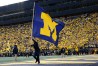 Michigan cheerleader waves blue flag with yellow M in stadium end zone