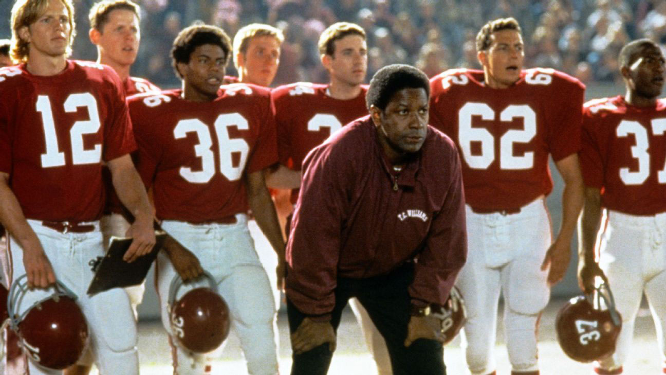 denzel washington stands in front of football players in red jerseys during a scene from remember the titans