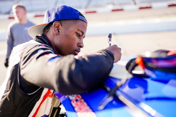 NASCAR driver Rajah Caruth writes with a pen on the roof of his car at a race track