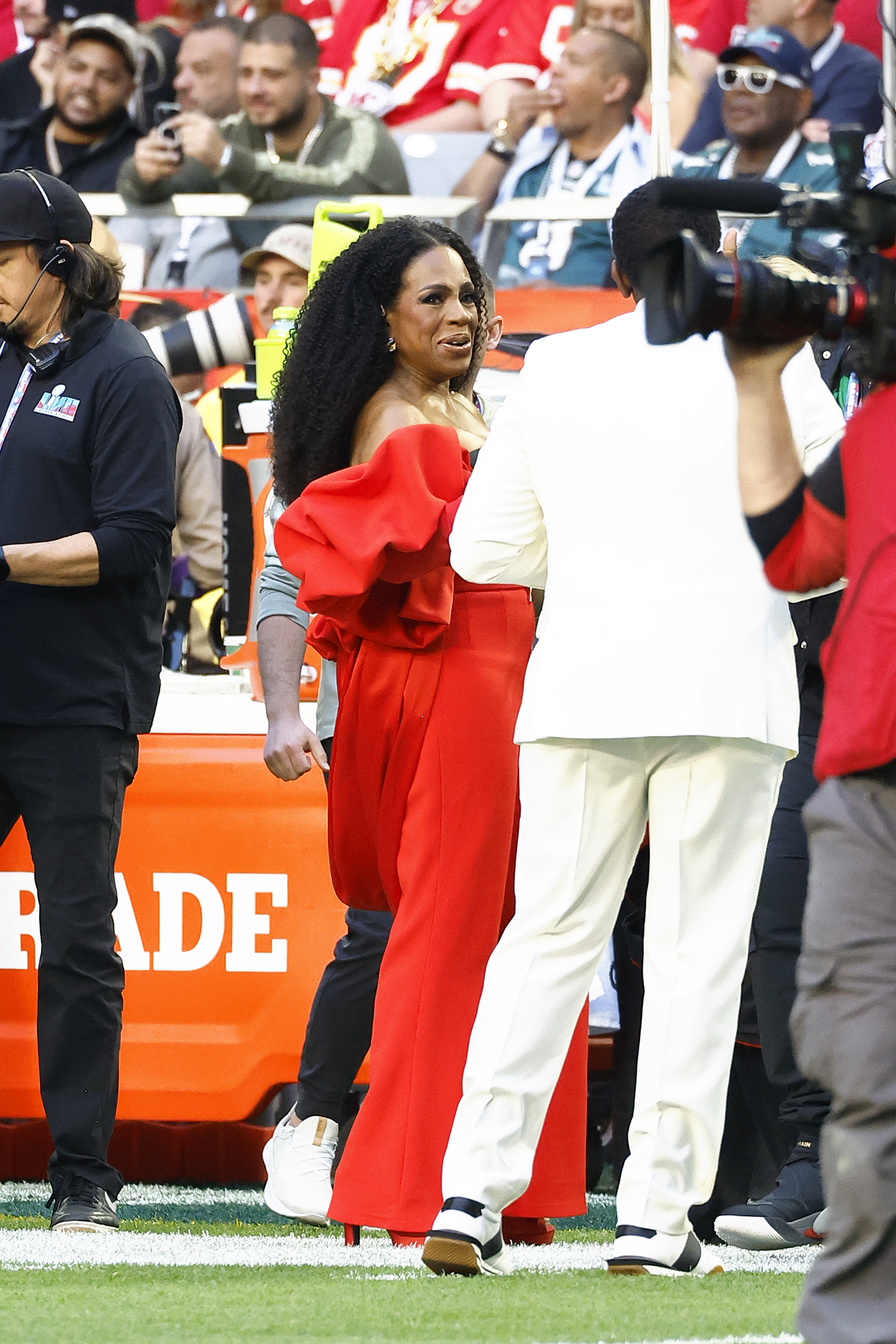 Sheryl Lee Ralph wears a stunning red dress with big fluffy sleeves on the sidelines as she talks to a man in a white suit. 