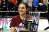 Georgia Amoore, wearing a maroon shirt, holds the ACC Tournament Championship trophy on the floor of the Greensboro Coliseum.